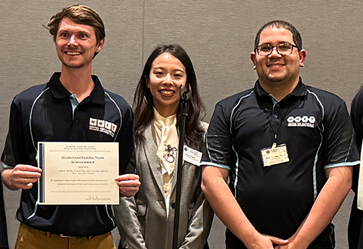 Three M-WET presenters smile at the camera after receiving an award for their research talk.