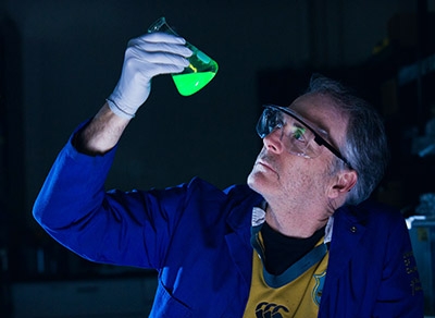 Professor Craig Hawker examines a vial of fluorescing green liquid.